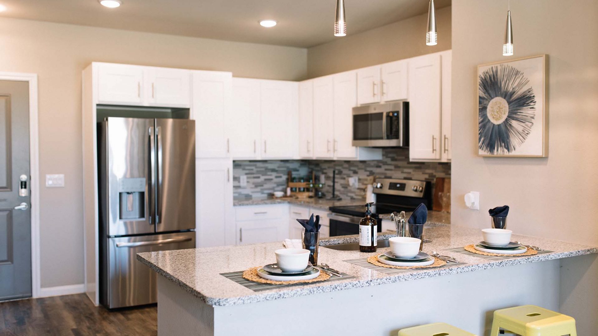 a kitchen with white cabinets and stools at The Gates at Meadow Place Apartments in Willow Park Texas