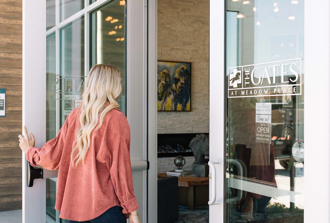 a woman walking into a building with a glass door at The Gates at Meadow Place